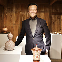 九谷焼赤絵細描の作家・米久 和彦さん。自身の作品が並ぶ展示空間で、赤と金の超絶技巧による唯一無二の器とともに