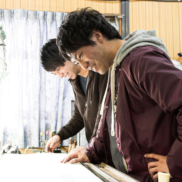 山梨・西桂のシルクカシミヤストールブランド「muto」の武藤 亘亮さん（右）と圭亮さん兄弟。工房の作業台で笑顔を見せる
